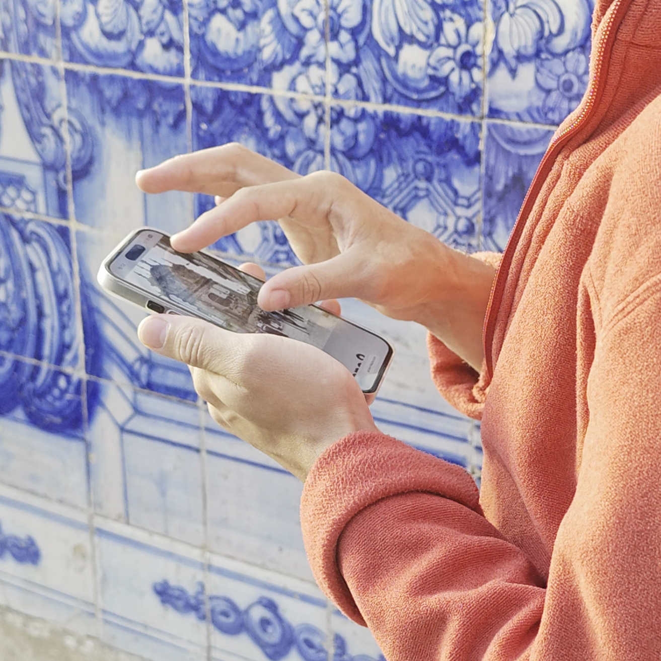 Hands holding a smartphone in front of a blue azulejo tiled wall in Porto